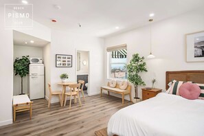 A bedroom with a bed, bedside table, lamp, and a window with a view. - Studio Suite at Pismo Beach Club (Pismo Beach)