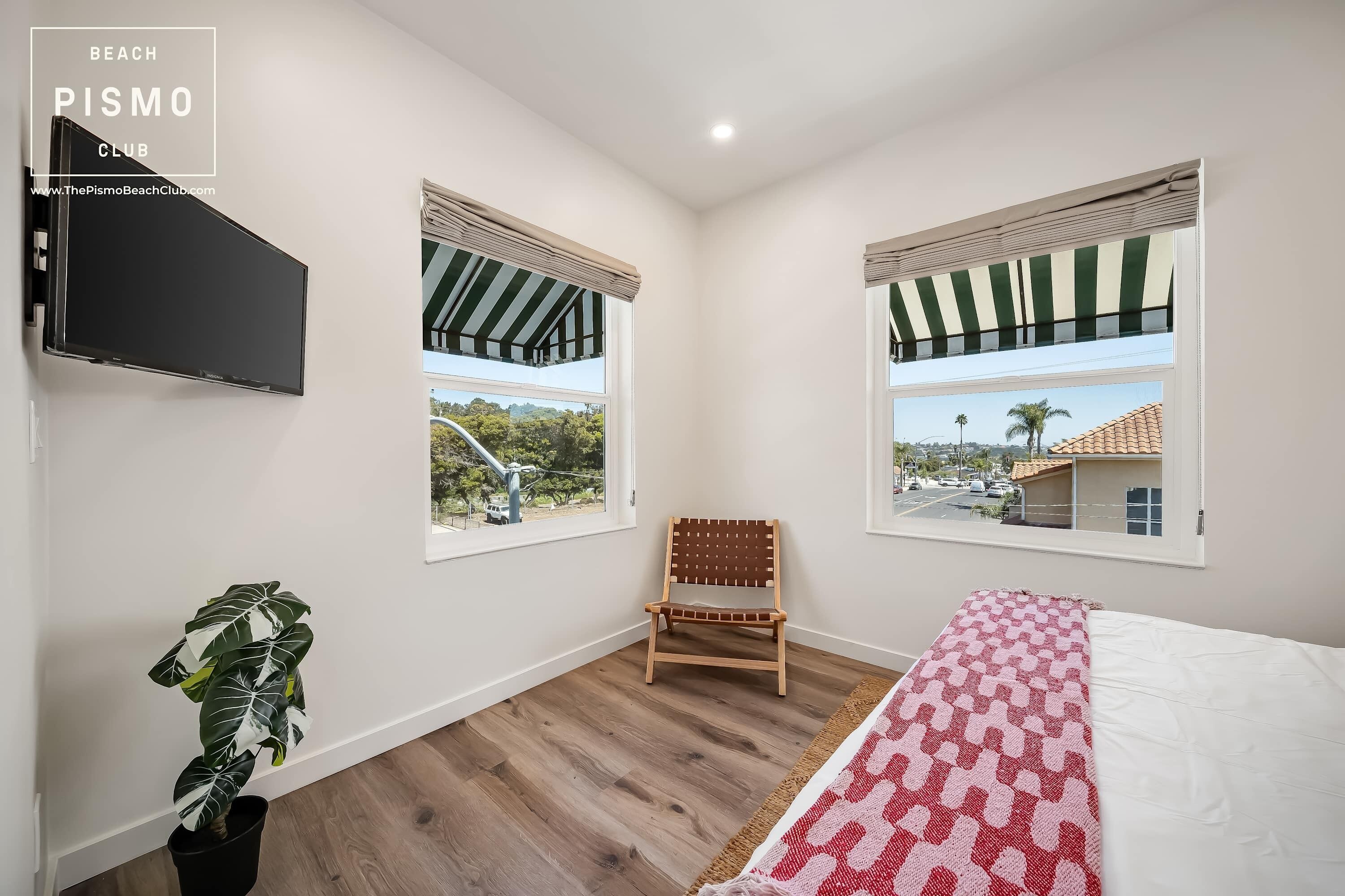 Quarto com cama, poltrona, televisão, janela com vista e planta.