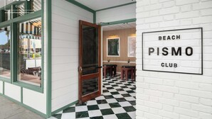 L’entrée du Pismo Beach Club se distingue par son sol à carreaux, sa porte en bois et une enseigne fixée au mur.