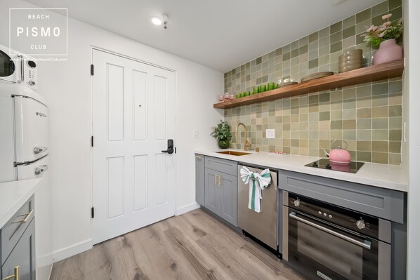 A kitchen with white cabinets, a stainless steel oven, a sink, and a backsplash with green tiles.
