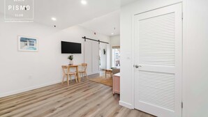 A modern interior with a wooden floor, a dining area with chairs and a table, a TV mounted on the wall, and a closed door.