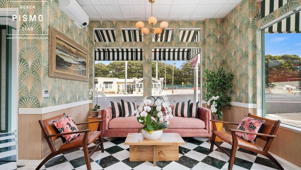 A lounge area with a checkered floor, a sofa, two armchairs, a coffee table with a plant, and striped awnings.