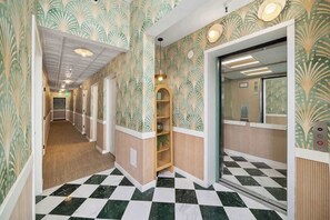 Un couloir d’hôtel avec un papier peint à motifs, un sol à carreaux et un comptoir d’accueil en bois.