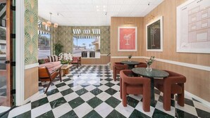 Un hall d’hôtel avec un sol à carreaux, un espace détente avec un canapé et des fauteuils, et un mur orné d’œuvres d’art encadrées.
