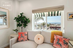 Un salón con sofá, una planta en maceta y una ventana con vistas a la playa y edificios.