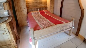 Un lit en bois, doté d’un cadre en bois et d’une couvre-lit à motifs rouges et blancs, se trouve dans une chambre rustique avec des poutres apparentes et une tête de lit en bois.
