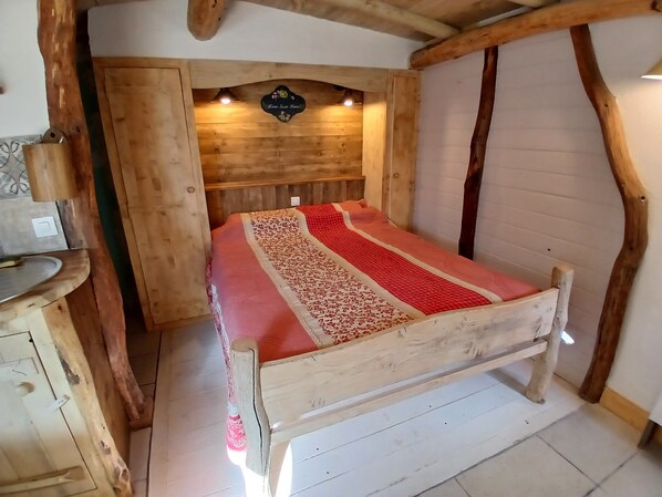 A wooden-framed bed with a red and white patterned bedspread in a rustic room with exposed wooden beams and a wooden headboard. - La Comté "Where the frogs sing (Bagnac-sur-Célé)