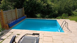 Une piscine rectangulaire avec une terrasse en bois et un toboggan bleu.