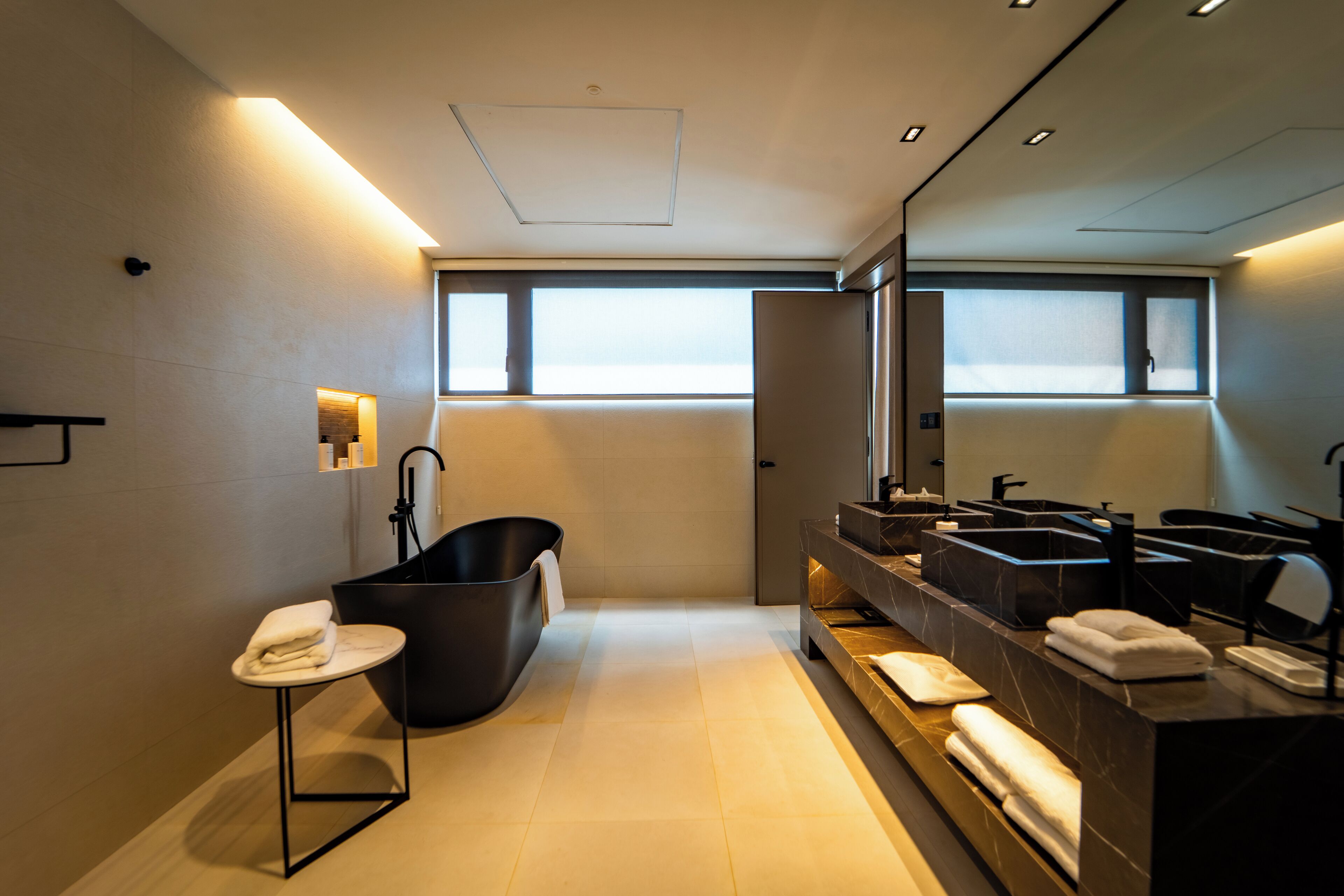 A modern bathroom with a freestanding bathtub, multiple sinks, and a small table with towels.