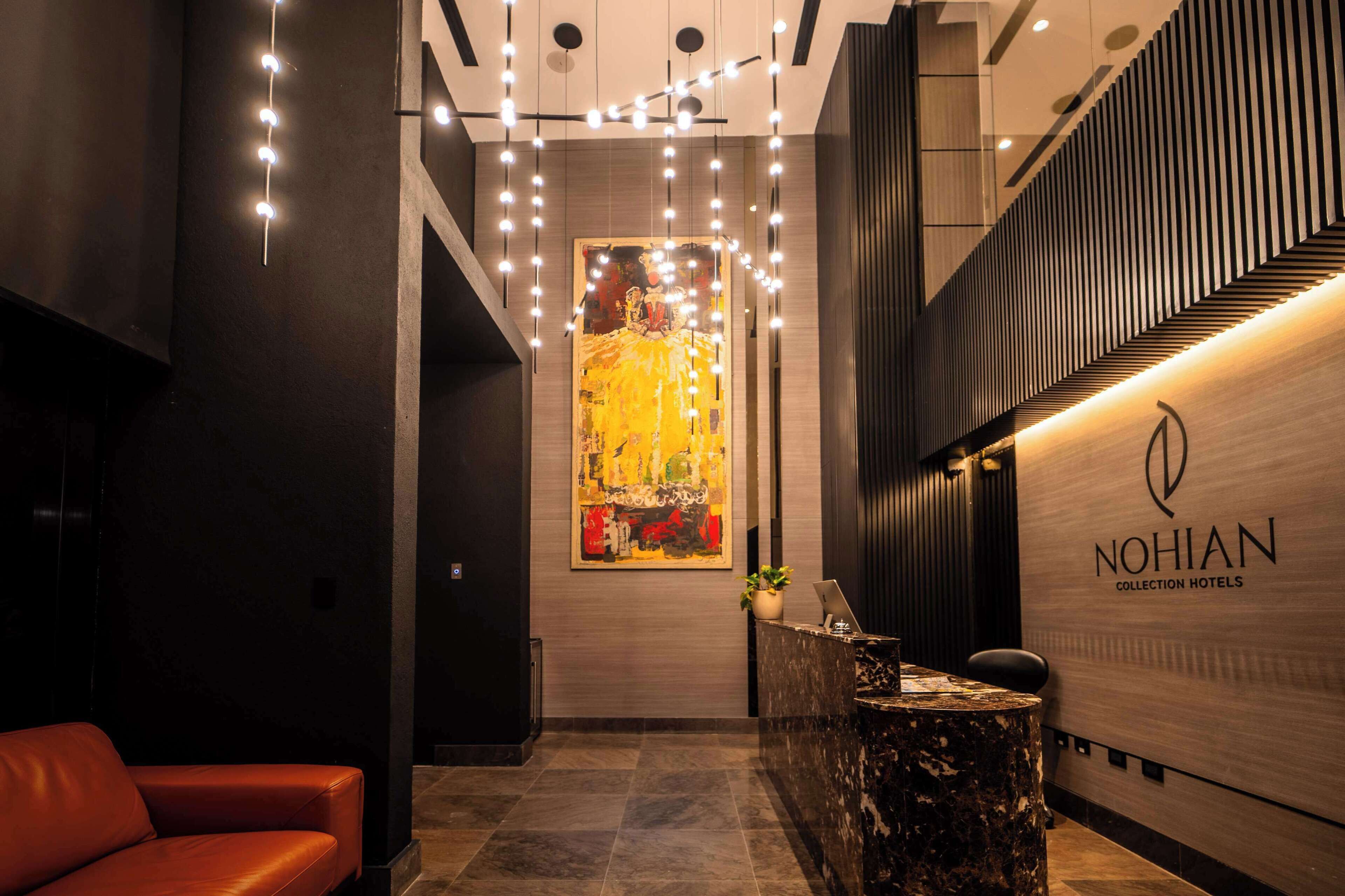 Een hotel receptie met een modern design, met een receptiebalie, een groot abstract schilderij en een zithoek met een rode bank.