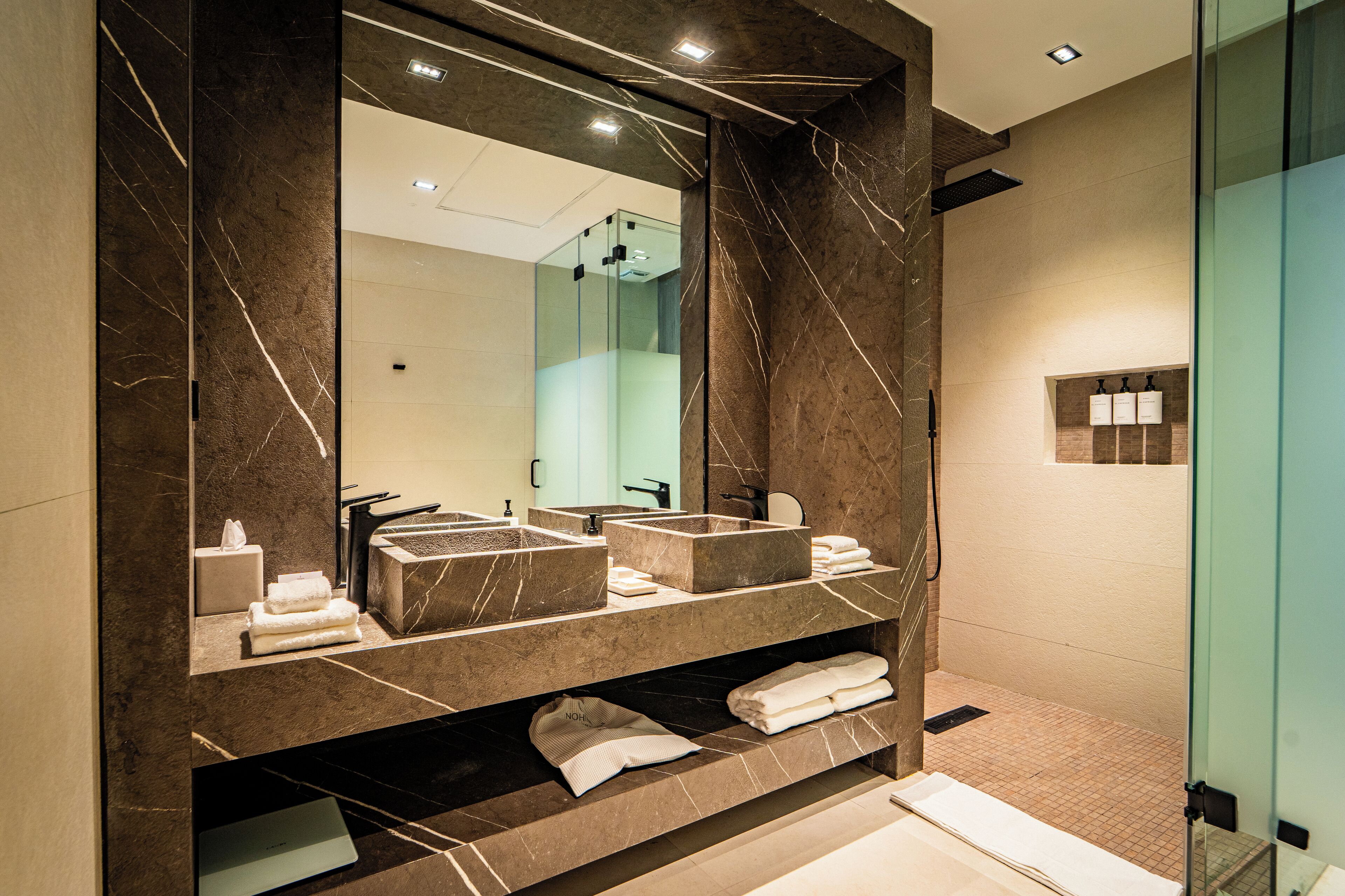 A modern bathroom with a large mirror, two sinks, and a shower area.