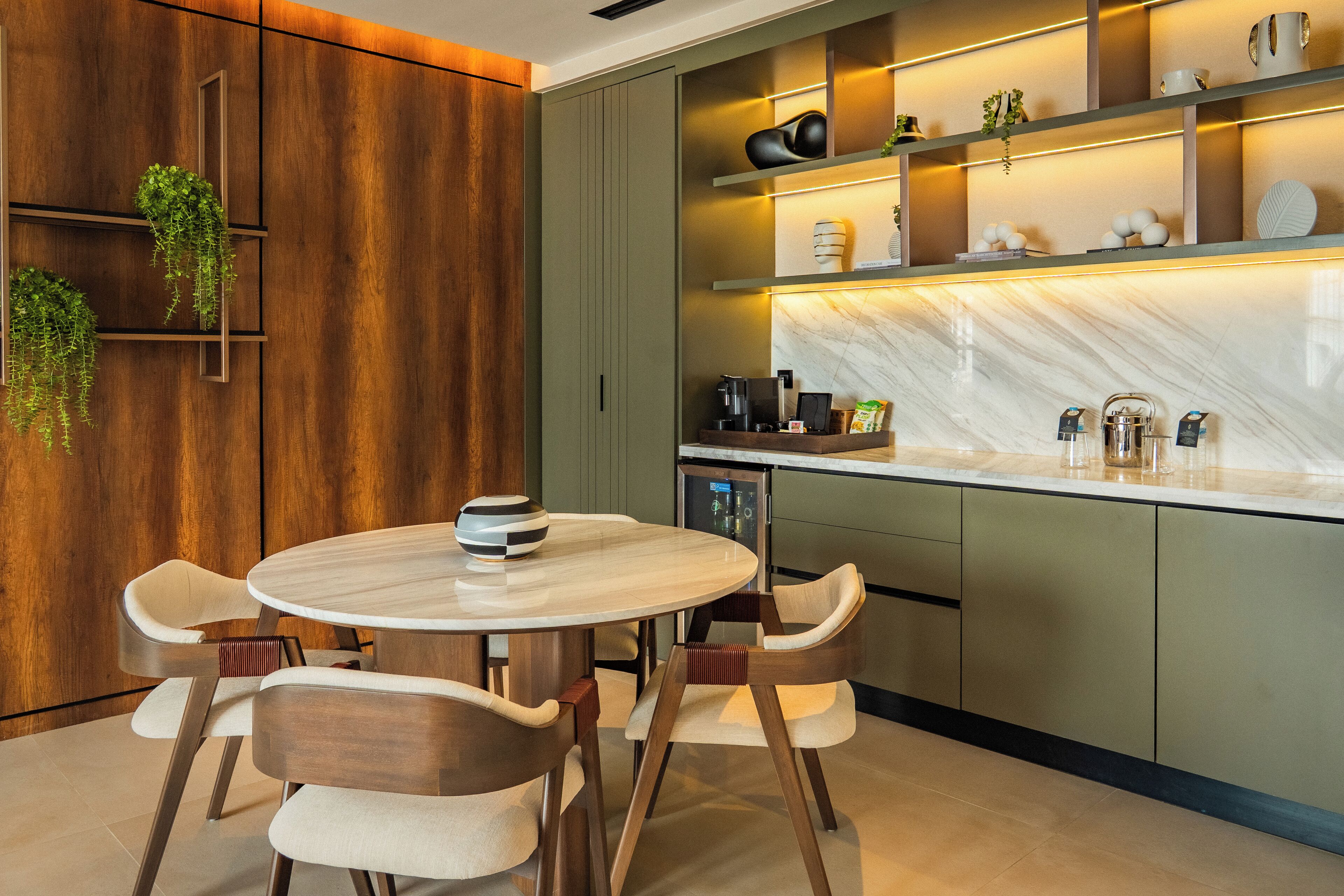 A modern kitchen with a round table and chairs, built-in shelves with decorative items, and a marble backsplash.