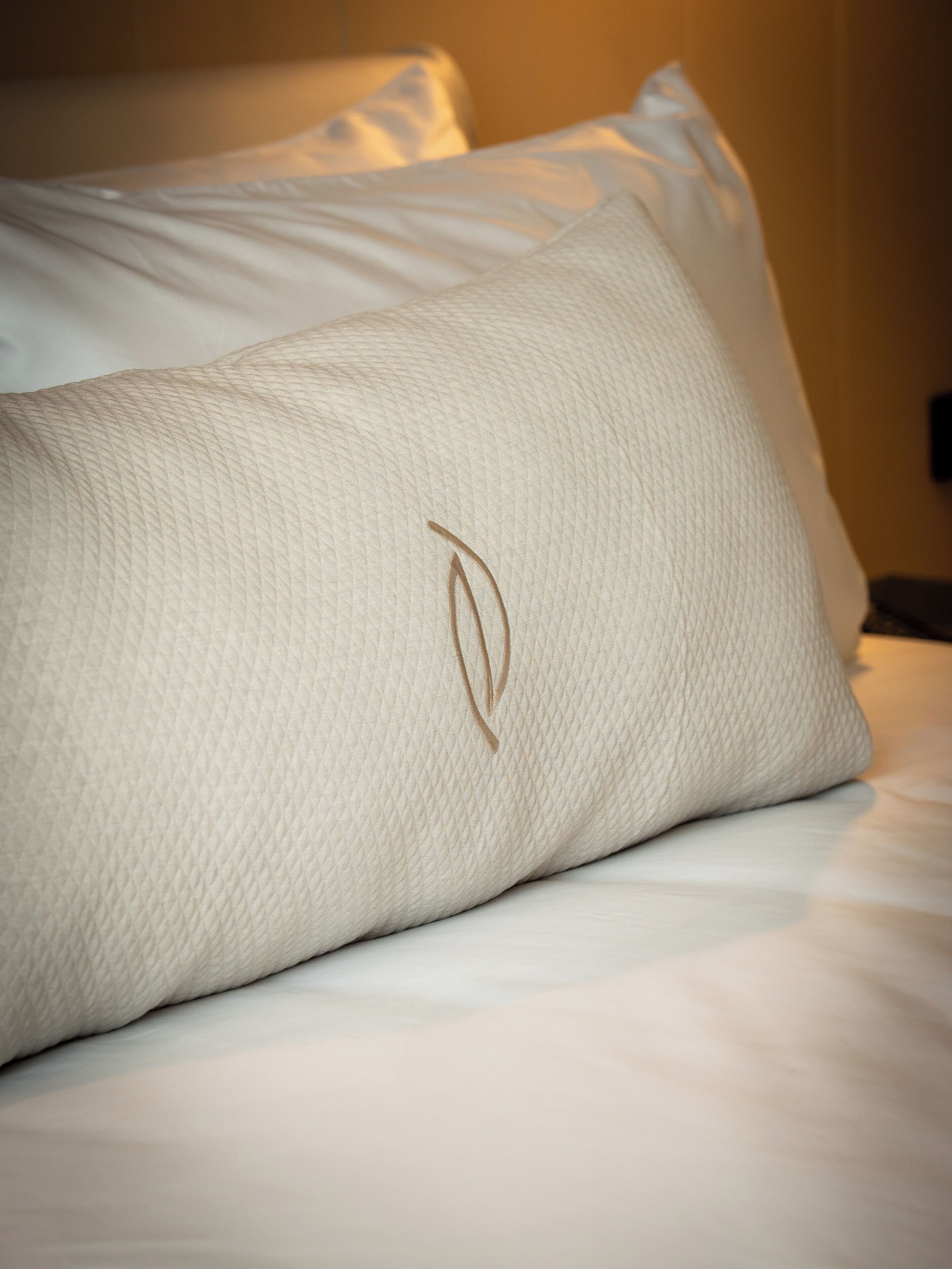 Un primo piano di un cuscino bianco con una semplice decorazione ricamata su un letto.