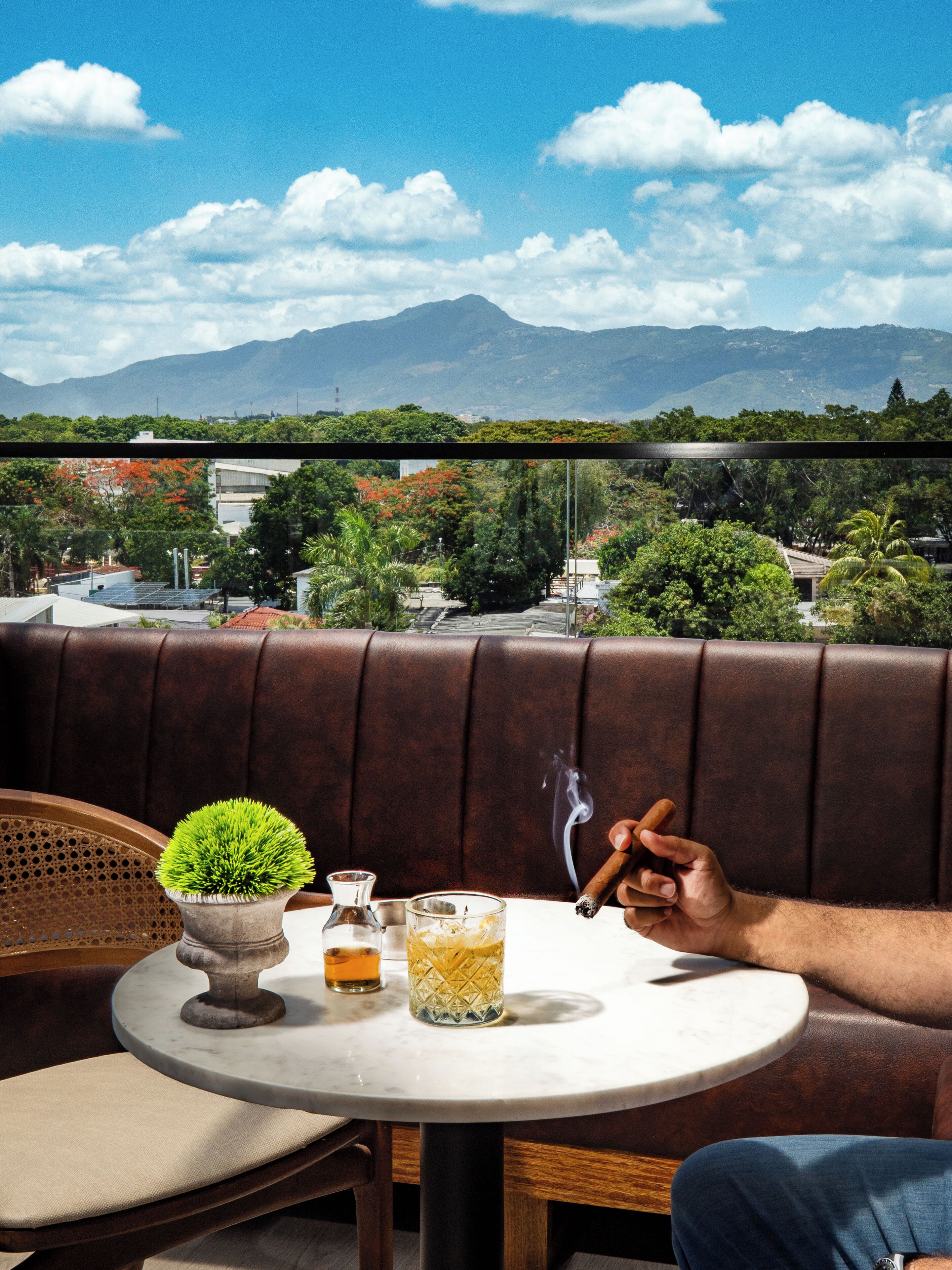 A person seated at a round table with a view of mountains and greenery in the background.