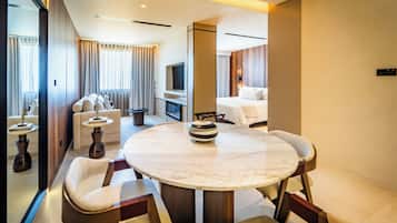 Una habitación de hotel moderna con una mesa redonda de mármol, dos sofás, un televisor y un minibar.