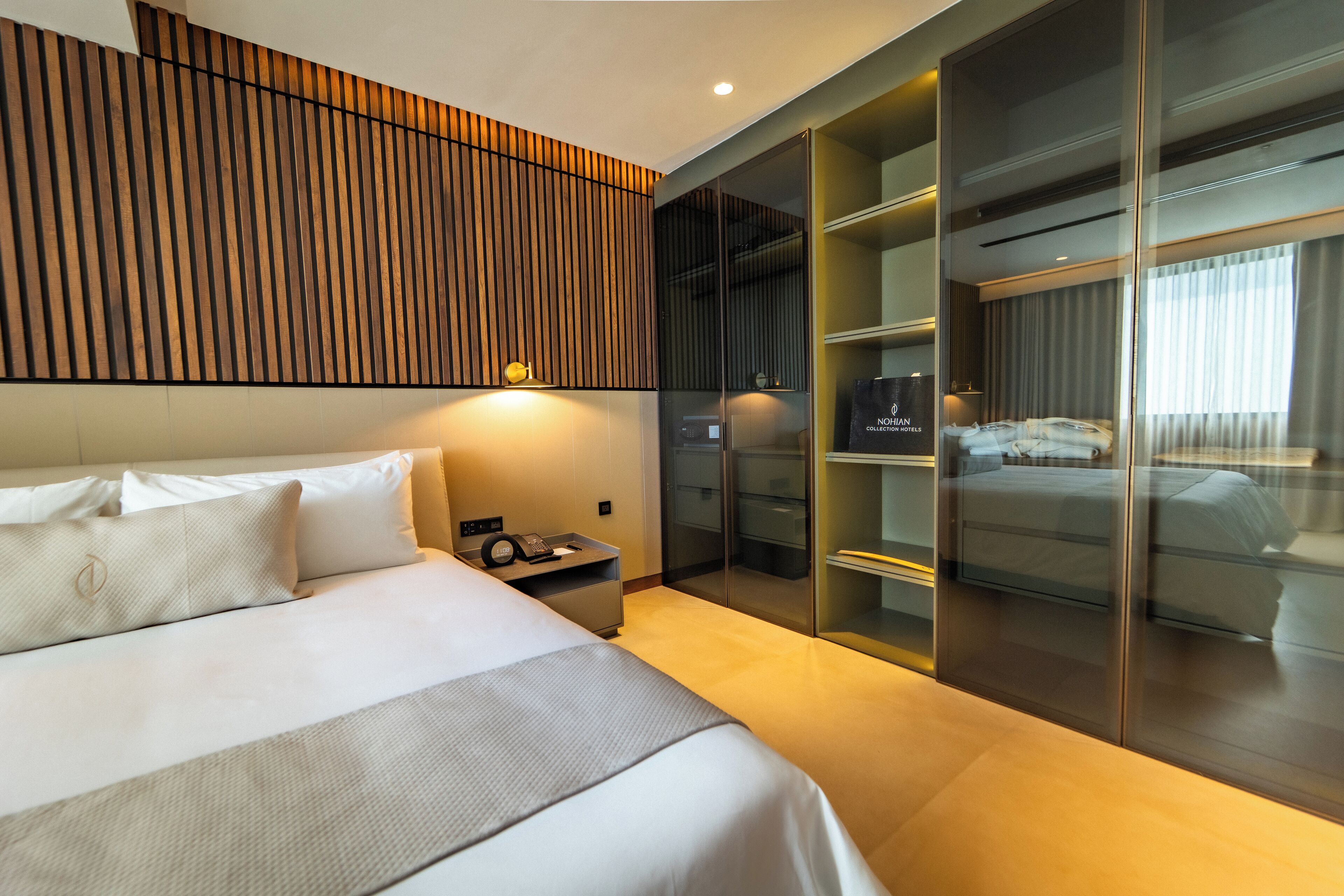 A modern hotel room with a large bed, a nightstand, a wardrobe, and a built-in closet with sliding doors.