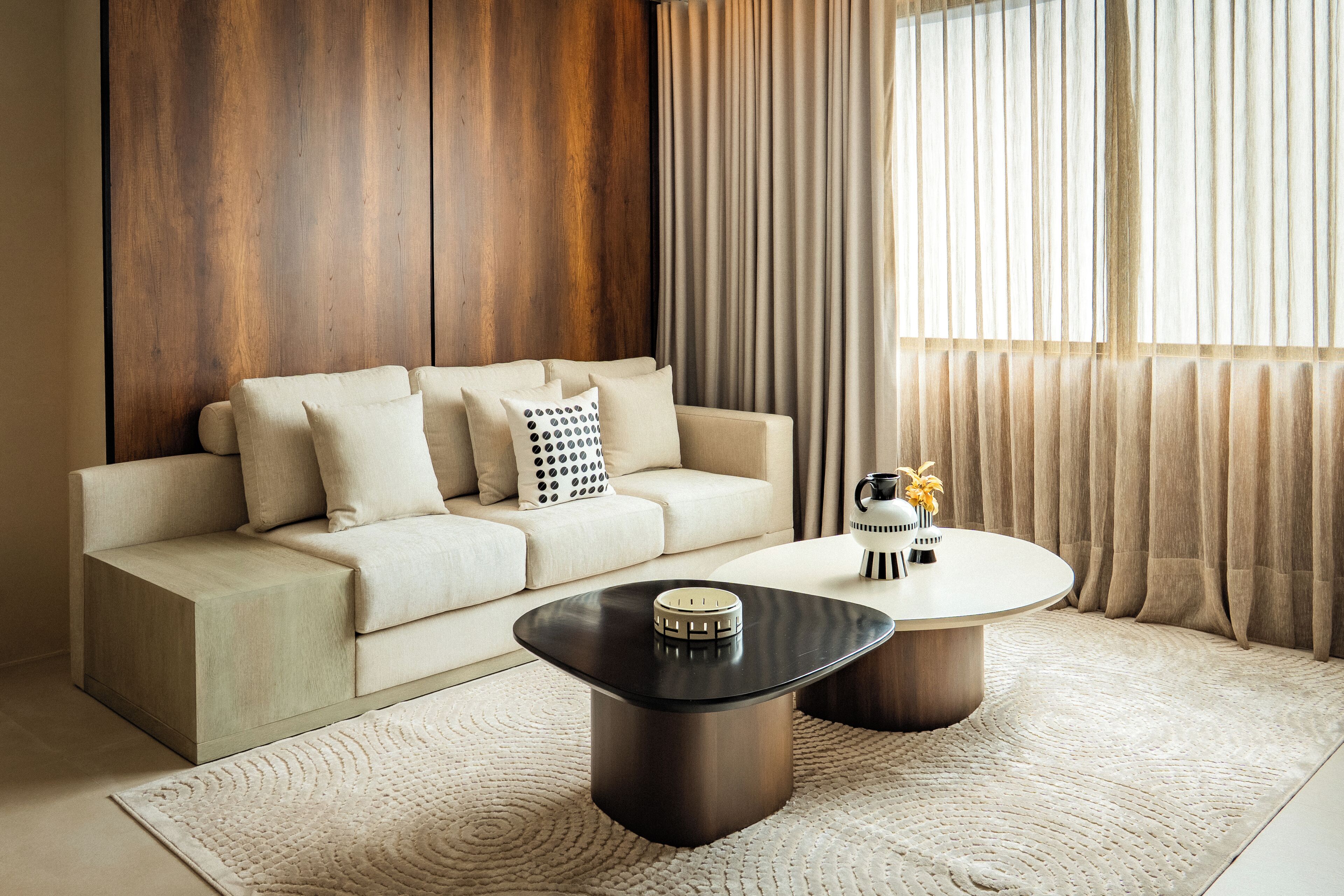 A modern living room with a beige sofa, two round coffee tables, and a wooden accent wall.