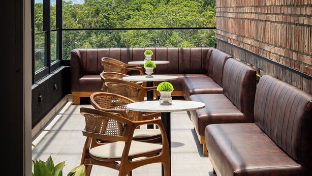 A balcony with a leather sofa, wicker chairs, and a small table with potted plants.