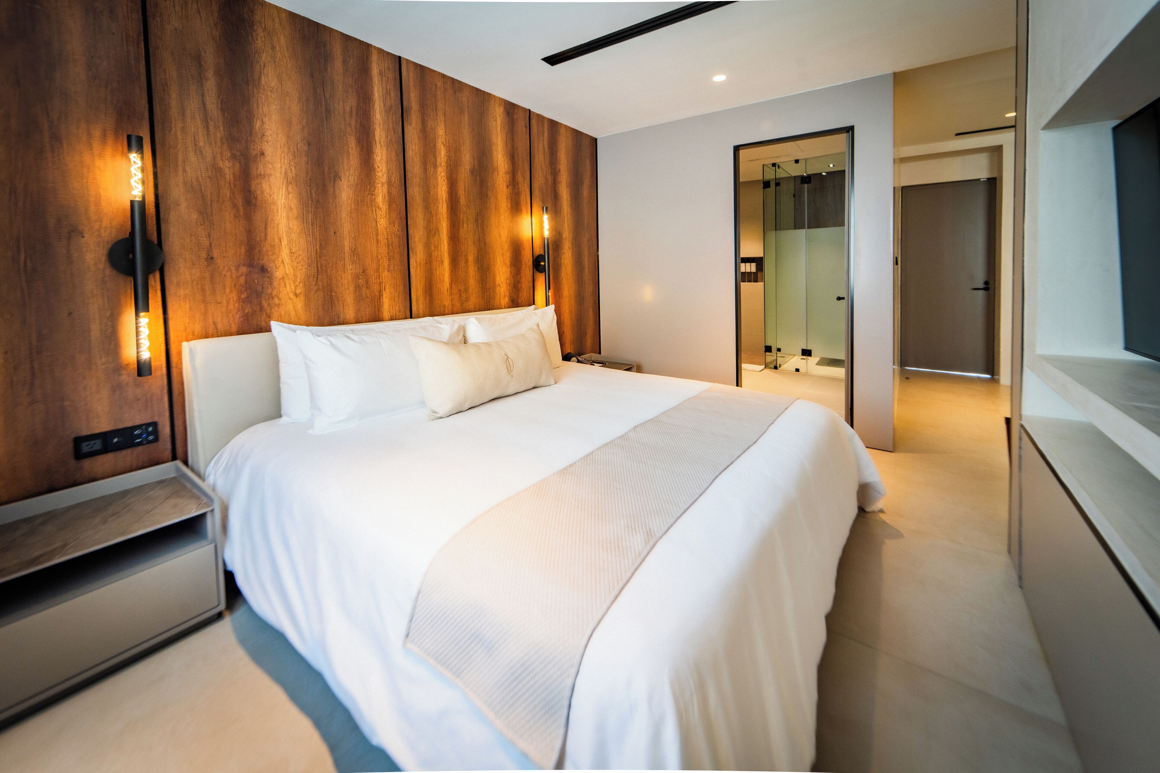 A modern hotel room with a large bed, wooden panel wall, and a mirror.