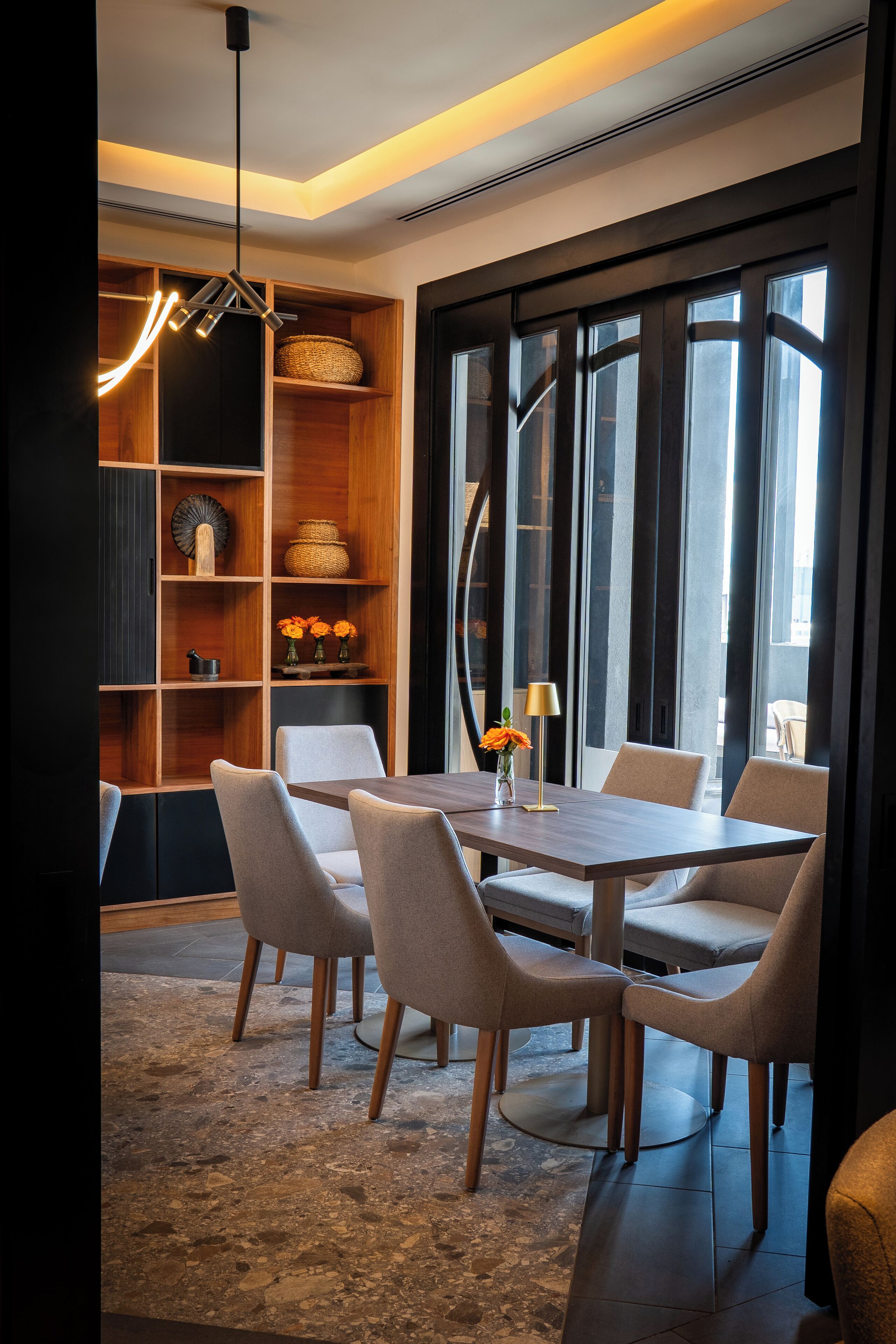 A modern dining area with a wooden table, six chairs, and a decorative shelf with baskets and vases.
