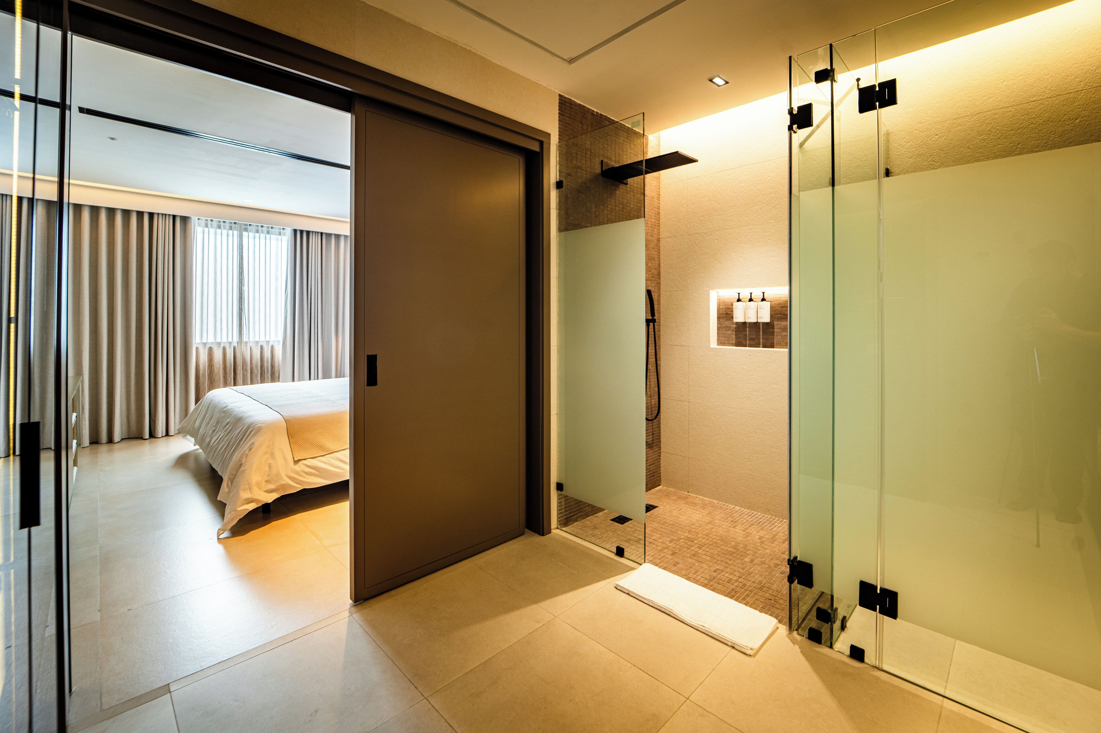 A modern hotel room with a bed, a glass partition, and a shower area.