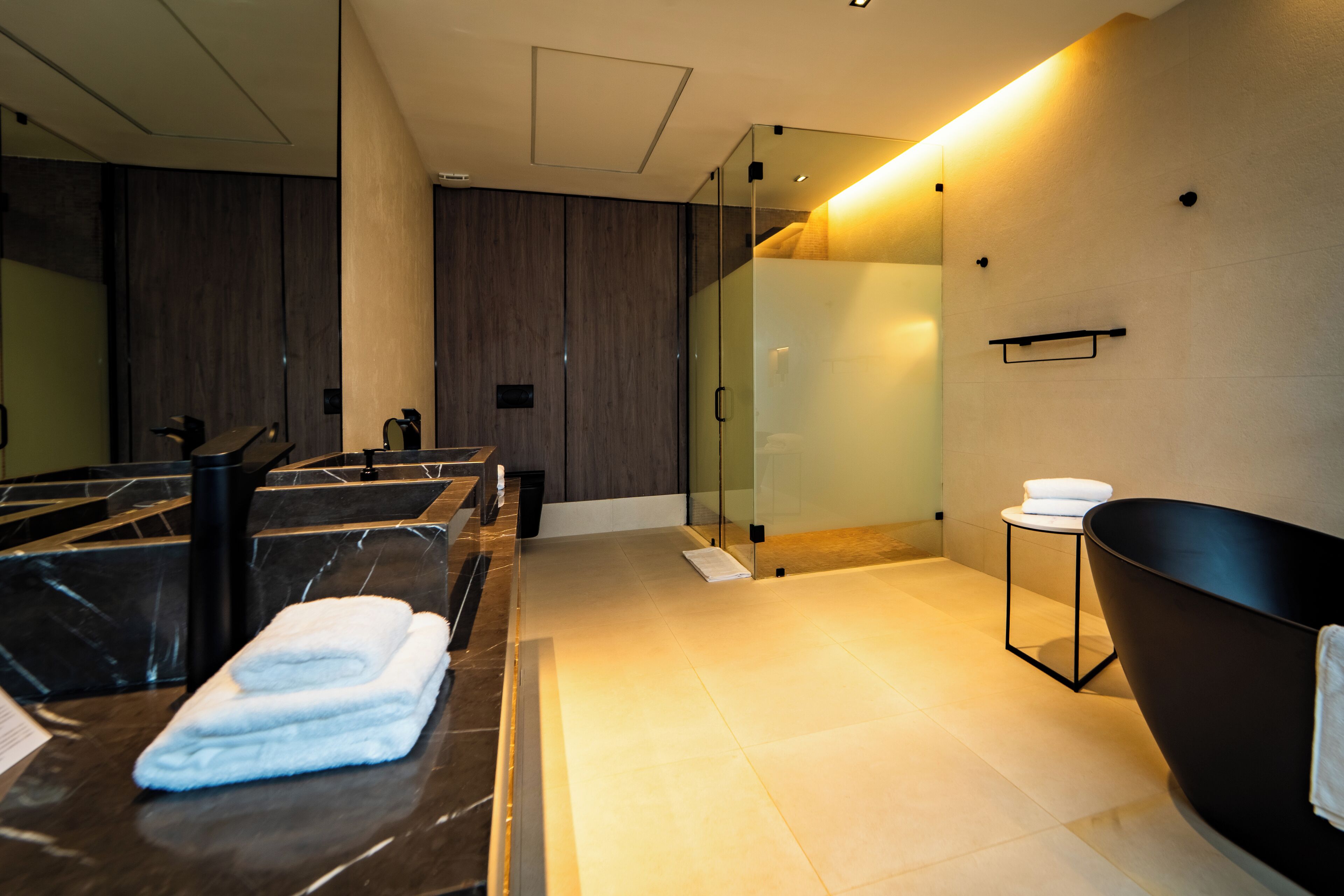 Une salle de bain moderne avec un grand miroir, une baignoire noire et une cabine de douche en verre.