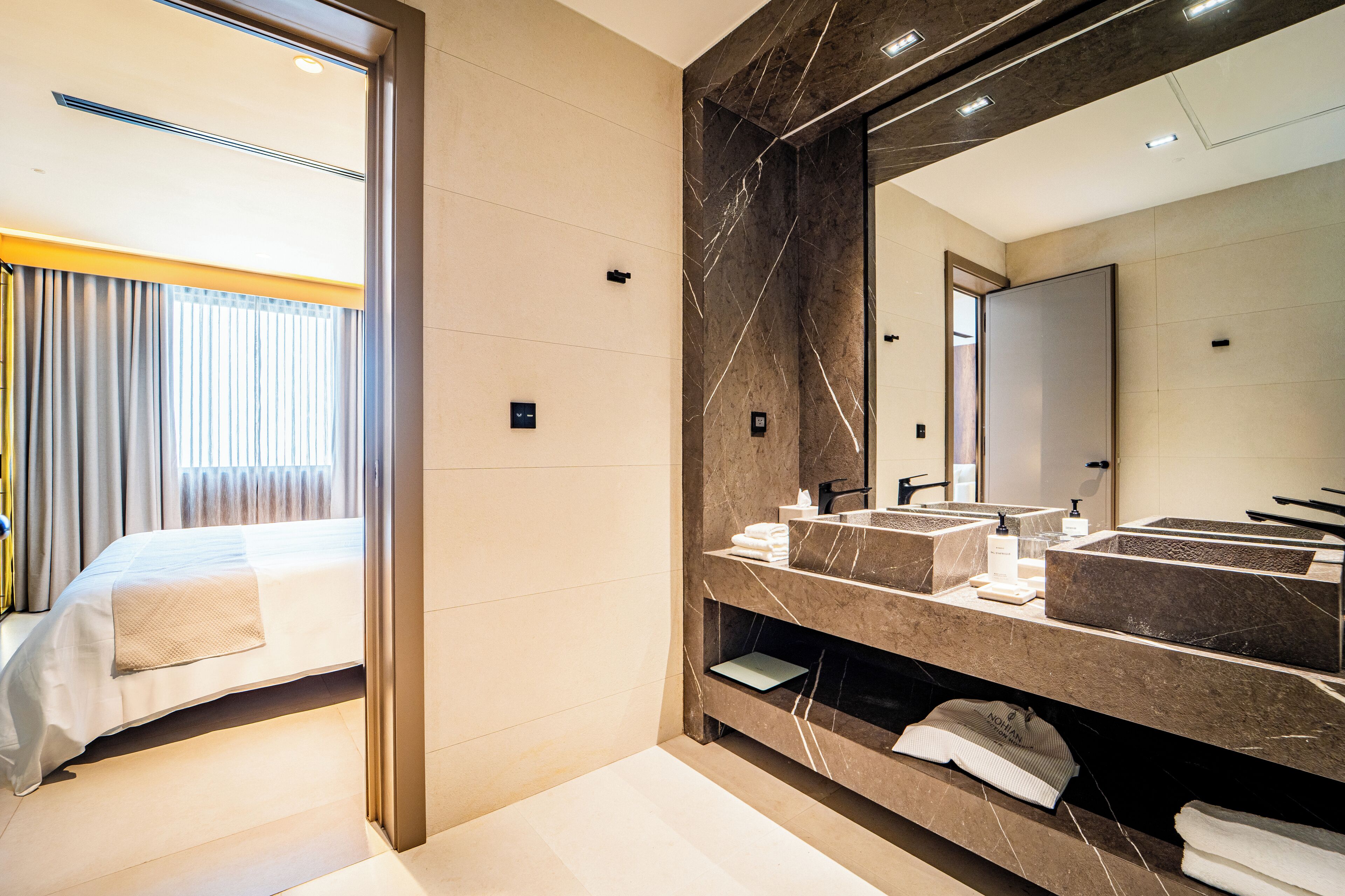 A modern hotel room with a large bed, a bathroom with a marble vanity, and a large mirror.