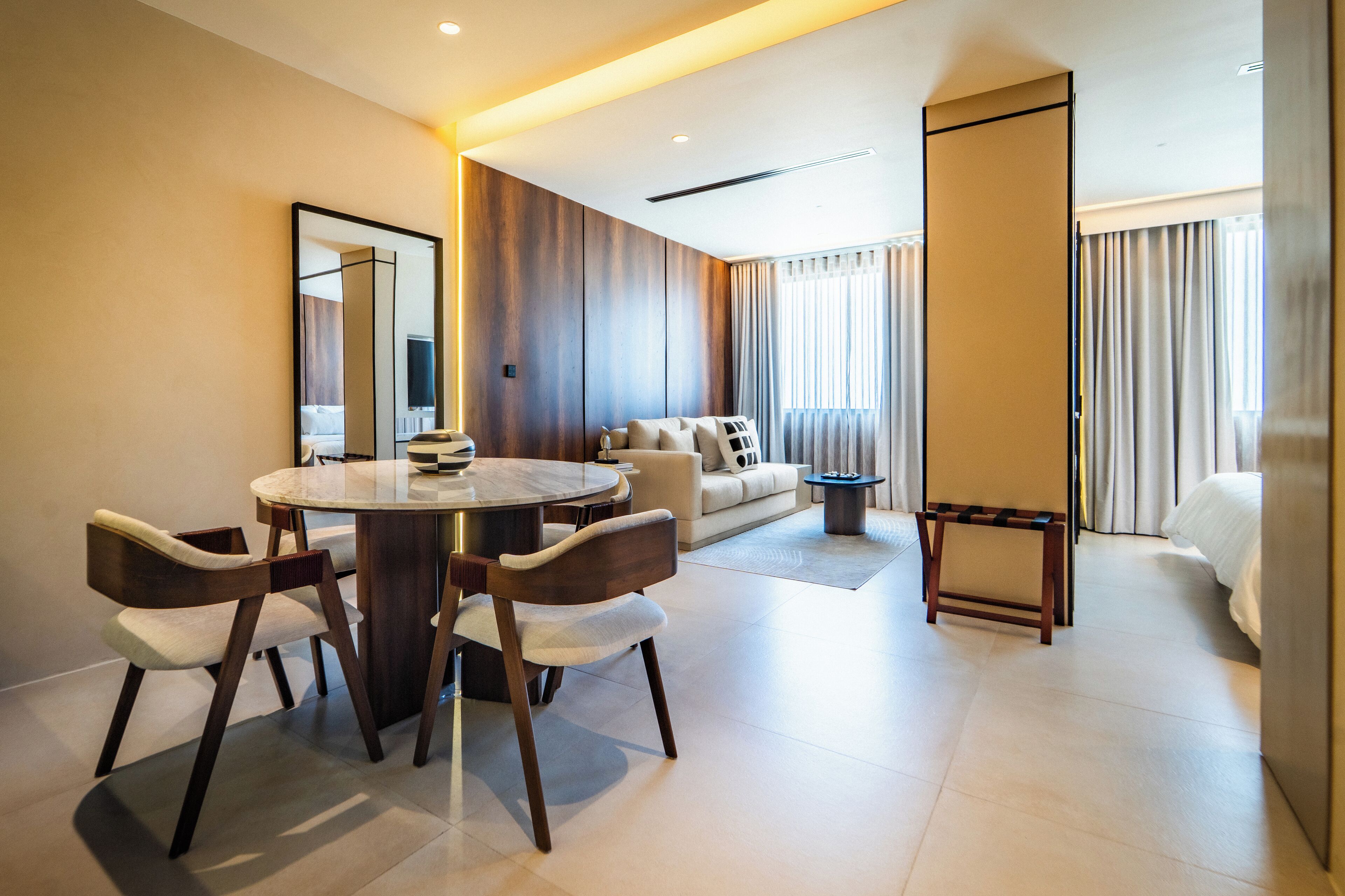 A modern hotel room with a dining area, a sofa, and a bed.