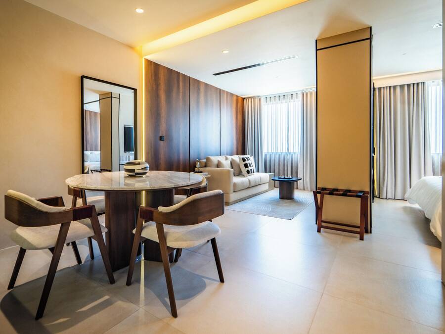 A modern hotel room with a dining area, a sofa, and a bed.