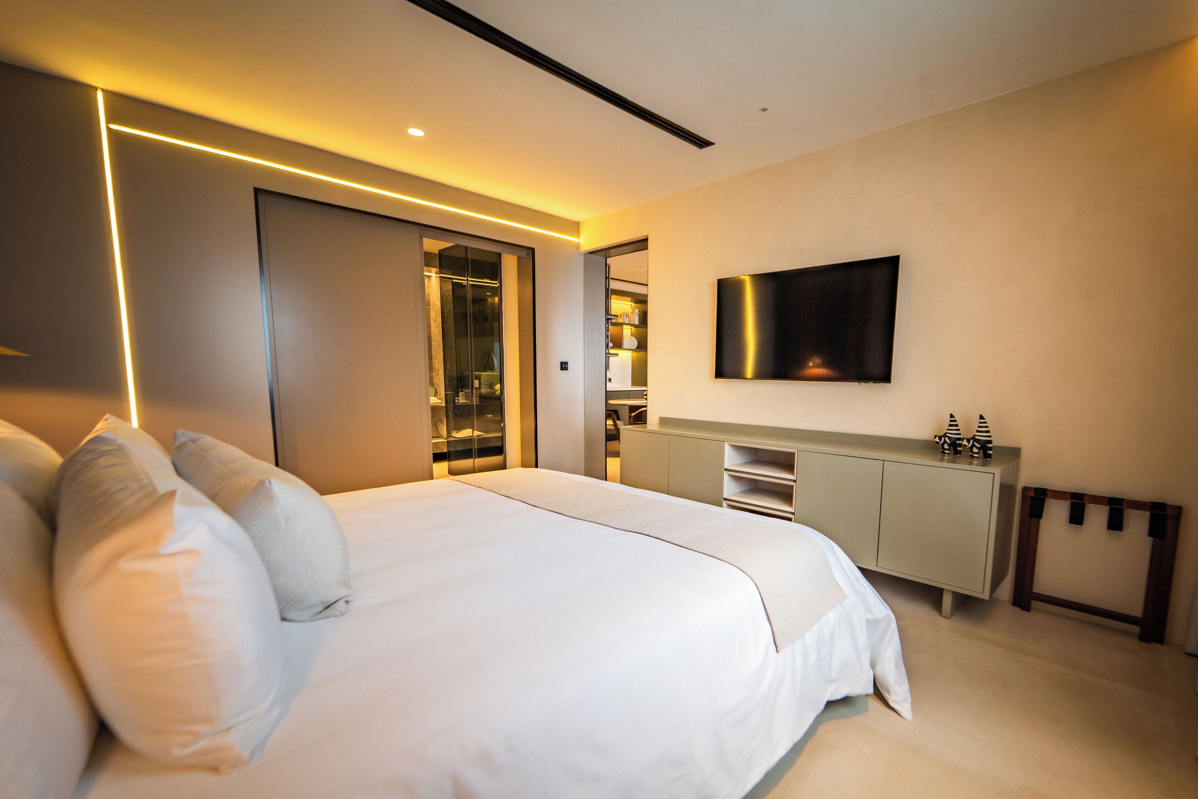 Un dormitorio moderno con una cama grande, un armario, un televisor montado en la pared y un vestidor.