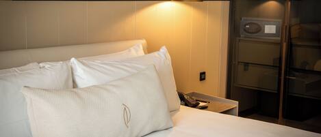 A neatly made bed with white linens and two pillows, a bedside table with a phone and a remote control, and a wall-mounted light fixture.