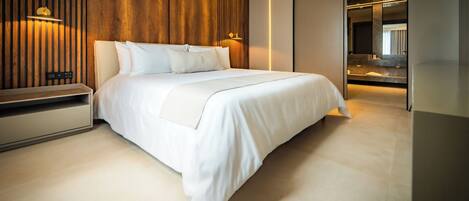 A modern hotel room with a large bed, wooden panel wall, and a bathroom visible through a sliding door.