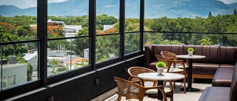 A rooftop terrace with a view of mountains, furnished with wooden chairs and tables, and a leather sofa.