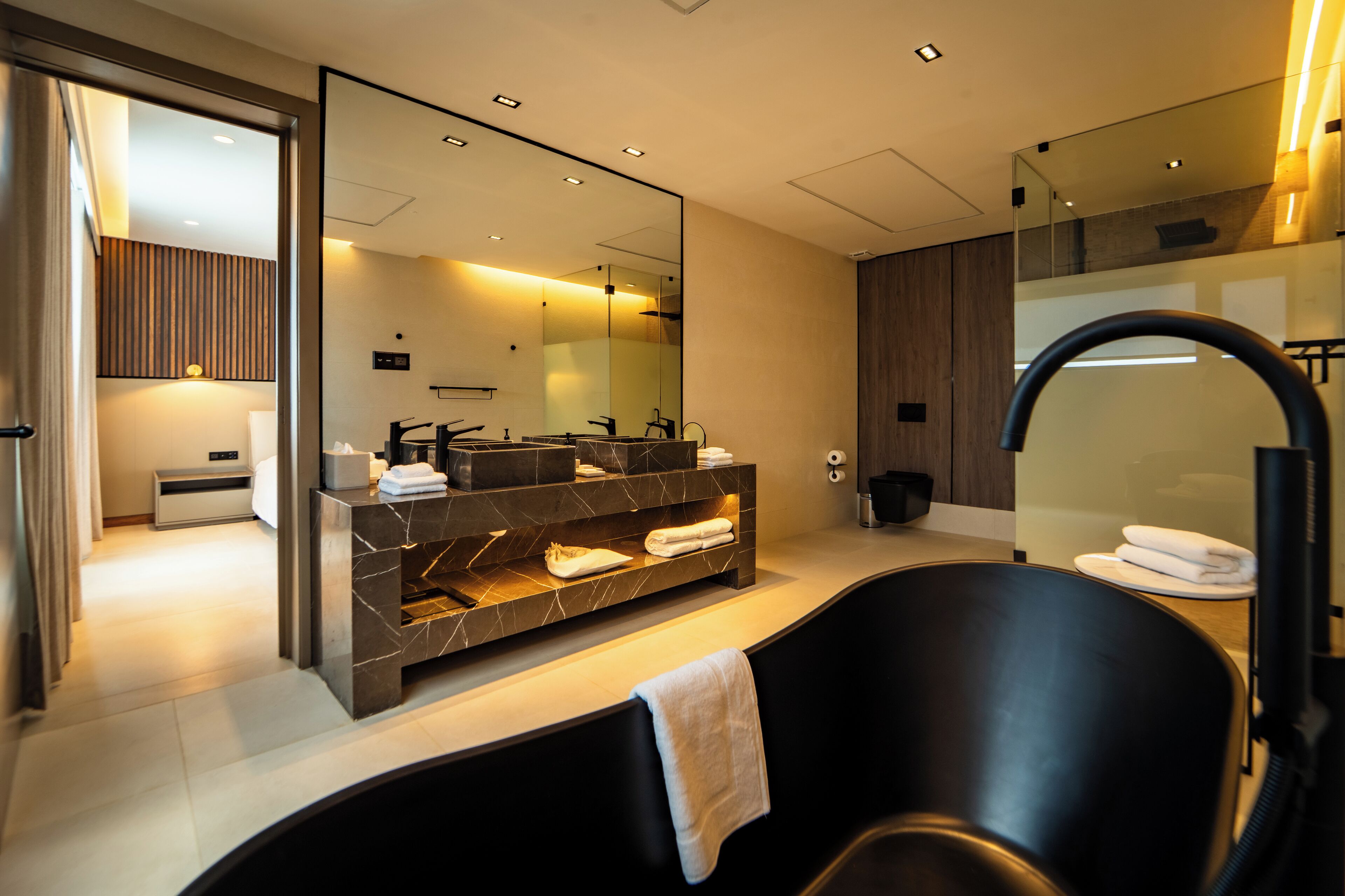 Un bagno moderno con un ampio specchio, una vasca da bagno nera e un mobile vanitario in marmo.