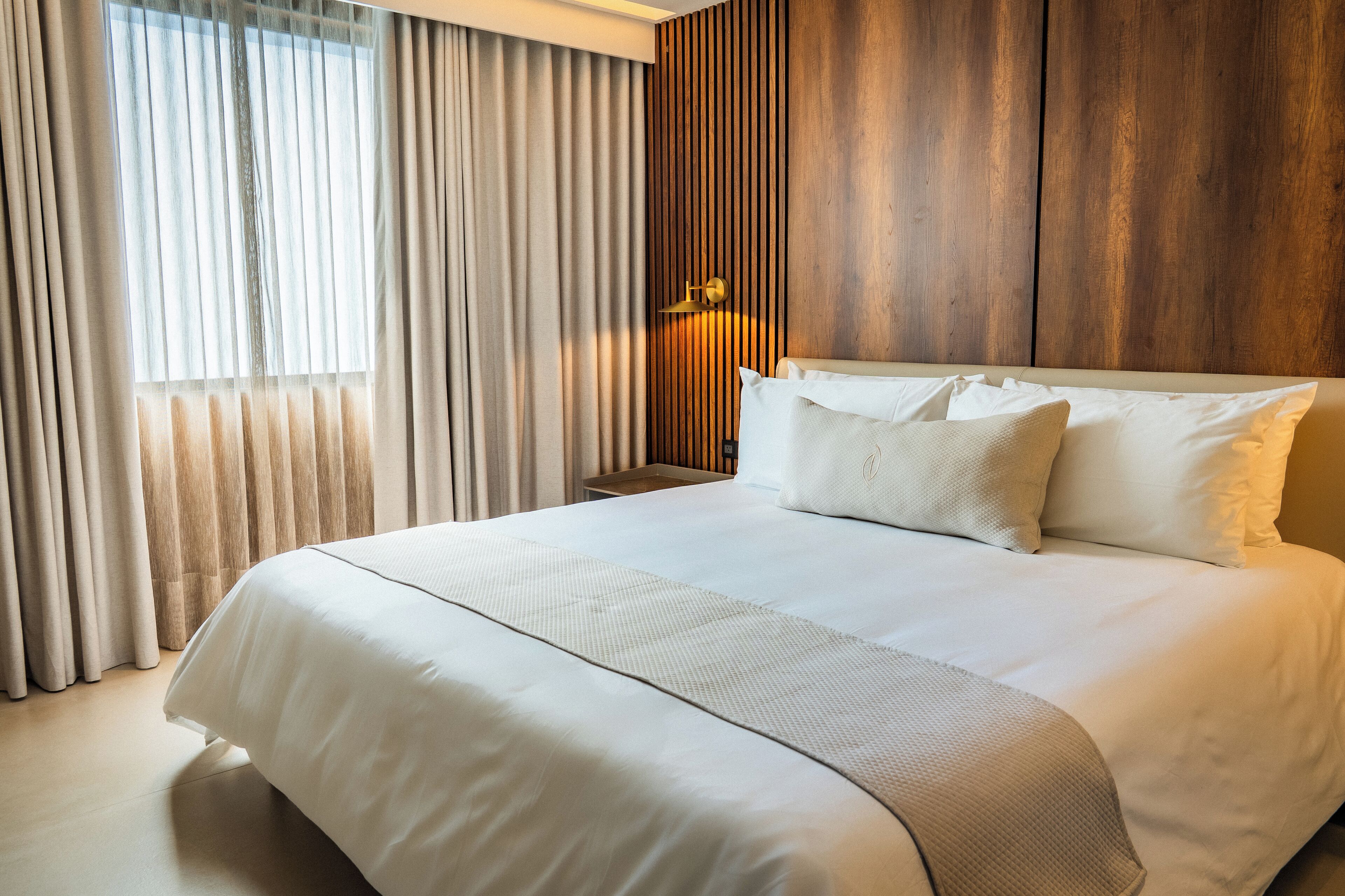 Une chambre d’hôtel avec un grand lit, un mur décoratif en bois et une fenêtre avec des rideaux.