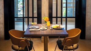 A dining area with a table set for two, featuring a vase with a single flower, a pitcher, and plates with food.