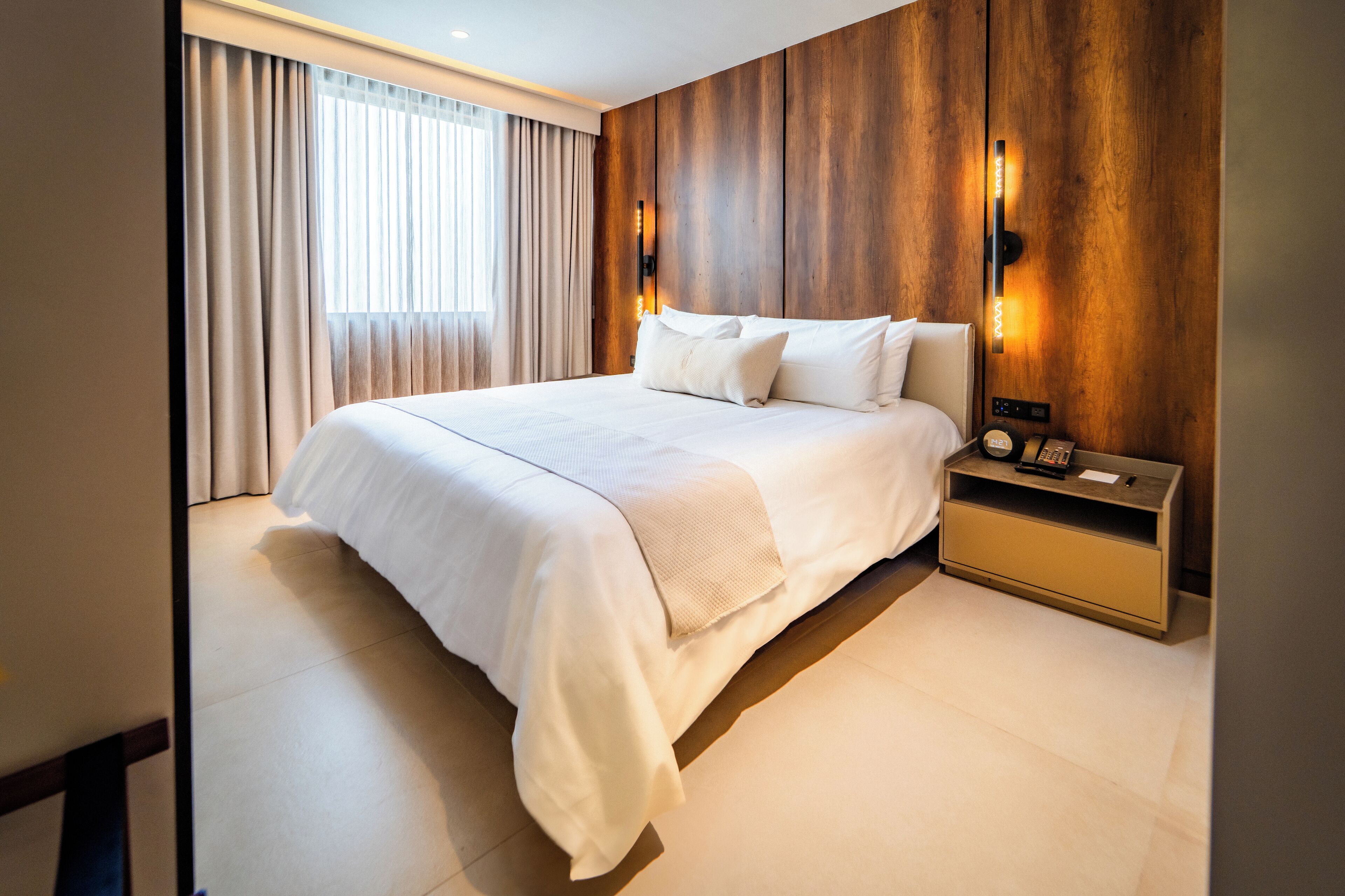 Un dormitorio de hotel moderno con una cama grande, paredes de paneles de madera y una mesita de noche con lámpara.