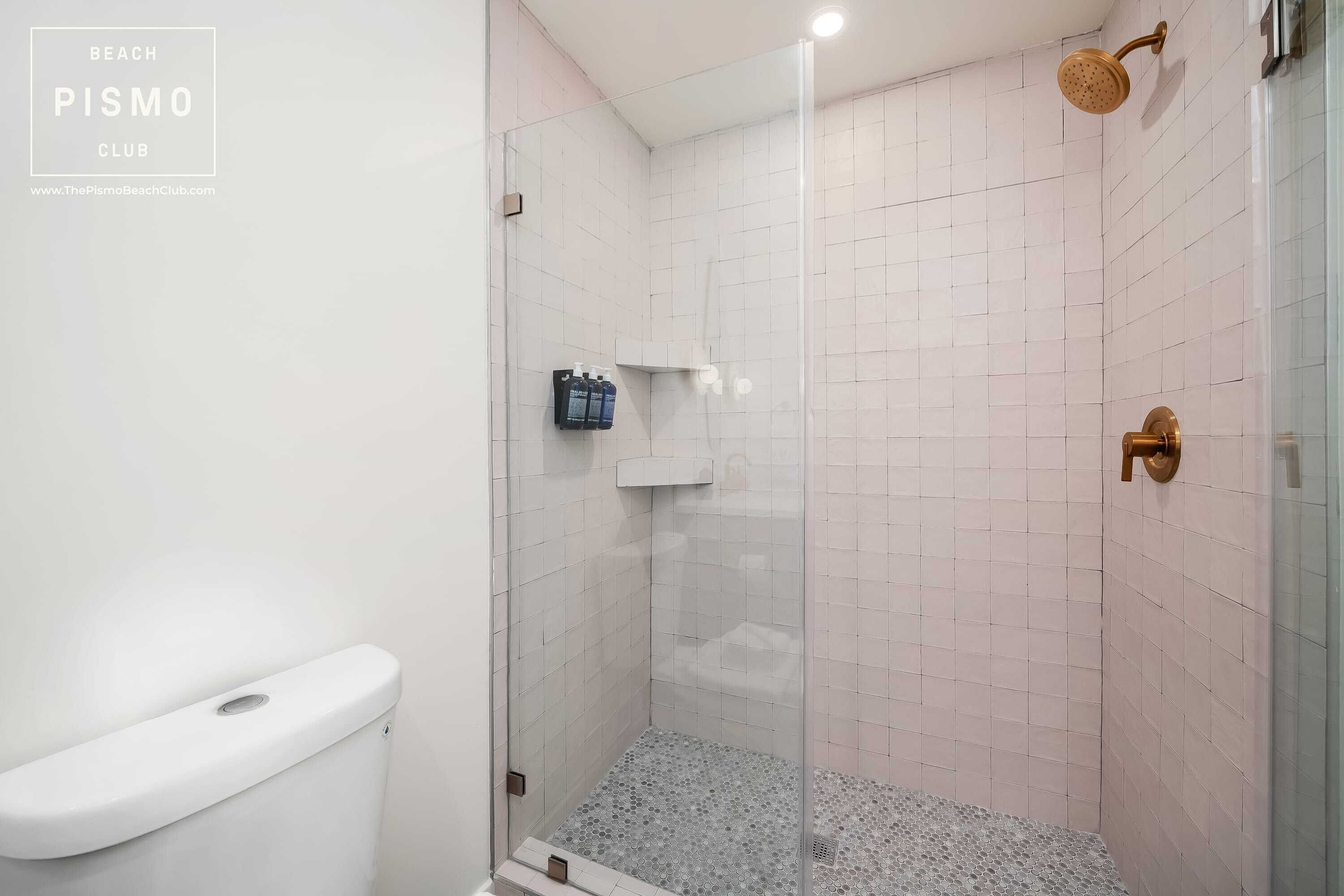A shower with a glass door, white tiled walls, and a toilet.