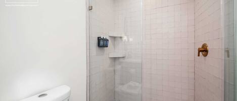 A shower with a glass door, white tiled walls, and a toilet.