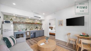 A modern, well-lit room with a kitchenette, a sofa, a round coffee table, and a TV mounted on the wall. - Deluxe Downtown View Suite at Pismo Beach Club (Pismo Beach)