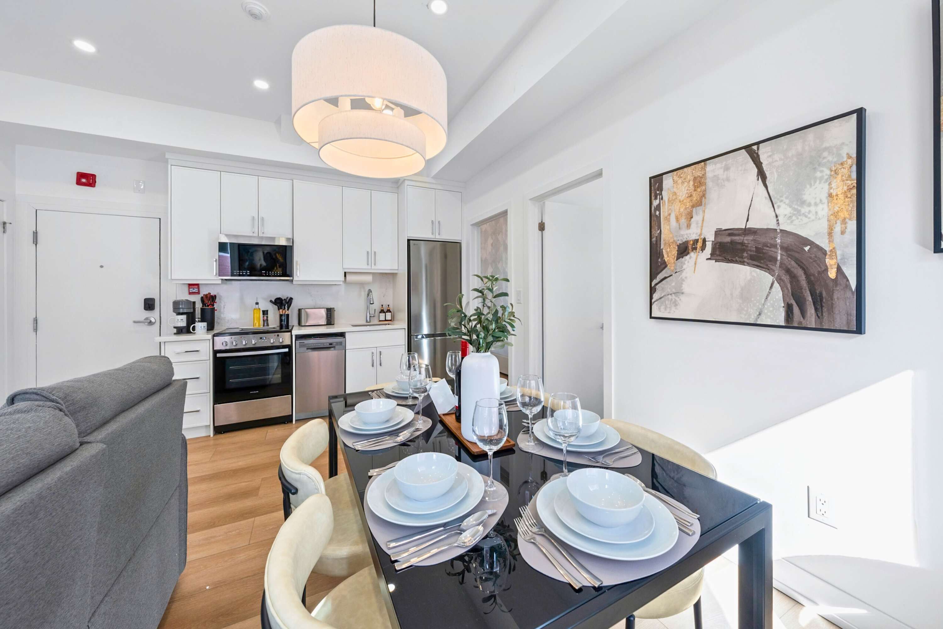 Een moderne keuken met witte kasten, een roestvrijstalen koelkast, en een eetgedeelte met een glazen tafel voor vier personen.
