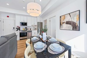A modern kitchen with white cabinets, a stainless steel refrigerator, and a dining area with a glass table set for four.