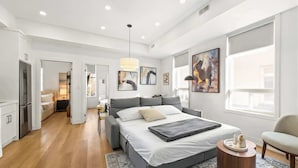 Een moderne slaapkamer met een groot bed, een nachtkastje, een stoel en kunstwerken aan de muur.