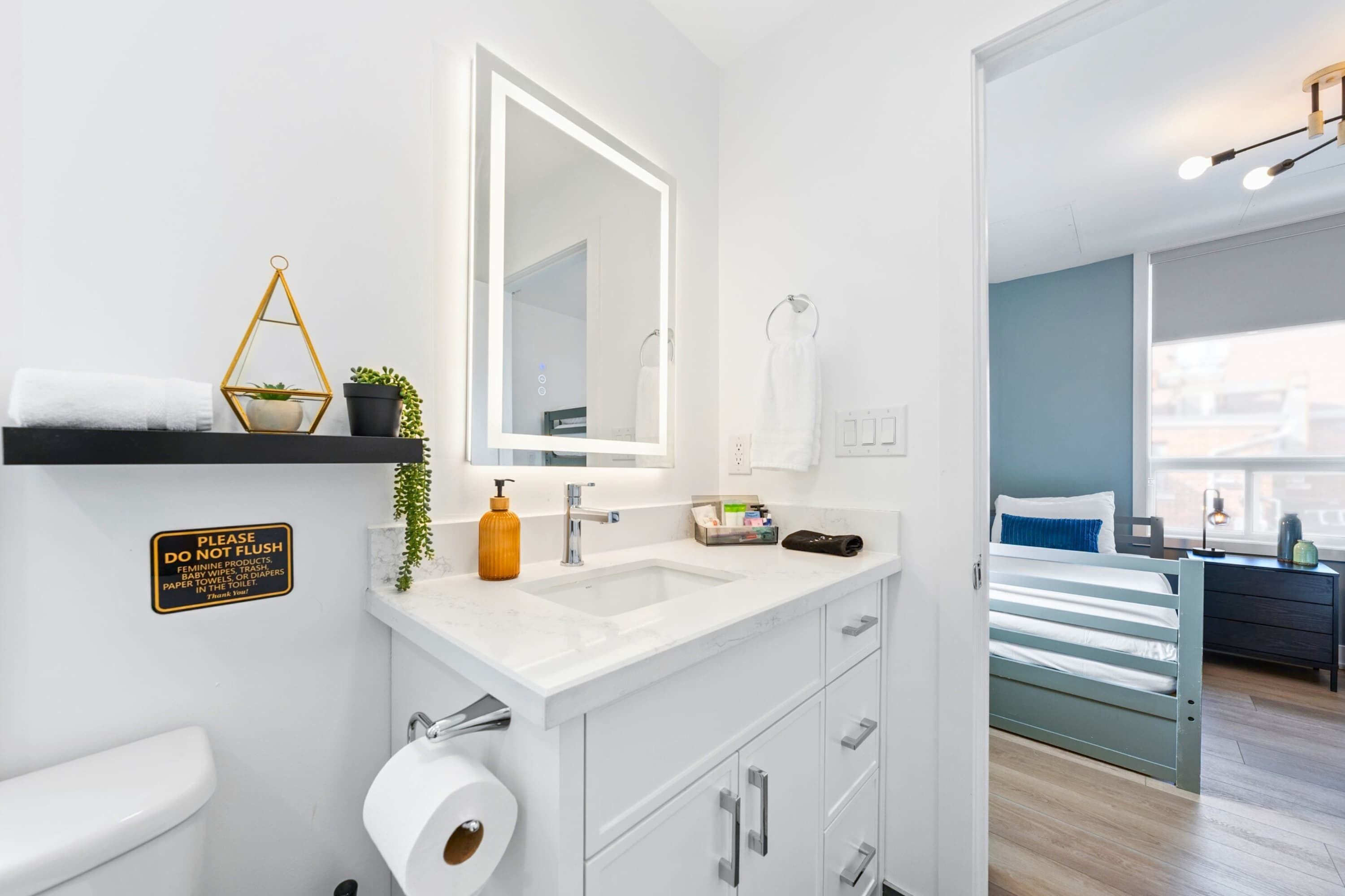 Un baño moderno con lavamanos, espejo, inodoro y un letrero que dice 'No tire papel'.