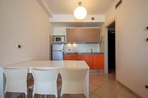 Une cuisine compacte avec un coin repas, comprenant une table et des chaises blanches, un four à micro-ondes, un réfrigérateur et des placards orange.
