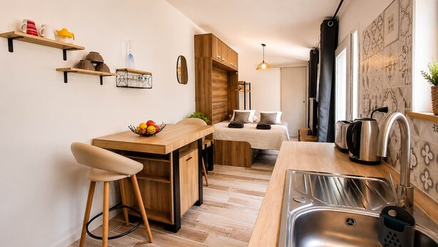 Cocina compacta con una isla de madera, taburetes, un lavamanos y un pequeño comedor.