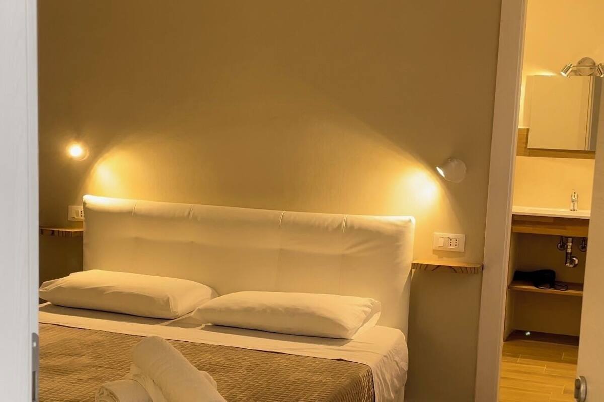 Ein ordentlich bezogenes Bett mit einer gesteppten Decke und zwei Kissen, einer Nachttischlampe und einer Wand-Klimaanlage.