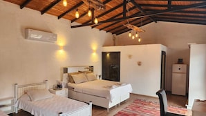 Un dormitorio con cama, mesitas de noche, un escritorio y una silla. El techo tiene vigas a la vista y lámparas colgantes.