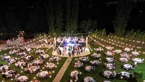 Evento al aire libre con mesas redondas dispuestas en semicírculo, un escenario central y luces colgantes.