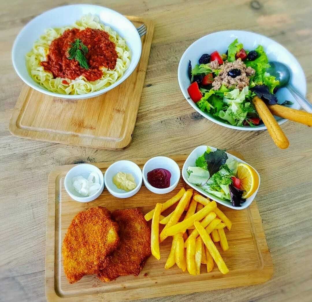 A meal consisting of pasta with tomato sauce, a salad with various vegetables and a protein, breaded fish, French fries, and small bowls of condiments.